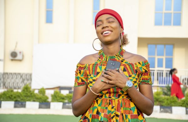 A beautiful African lady holding her phone to her chest filled with joy